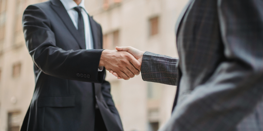 Two business professionals shaking hands in front of a modern building, symbolizing partnership and collaboration in digital marketing.