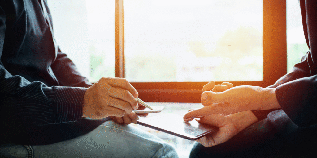 Two people sitting at a table, focused on a tablet, discussing digital marketing strategies and course options.