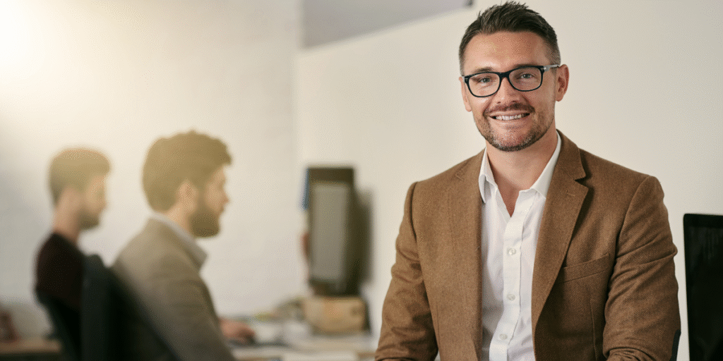 A smiling man in glasses sits at a desk, suggesting a positive atmosphere for learning digital marketing skills.
