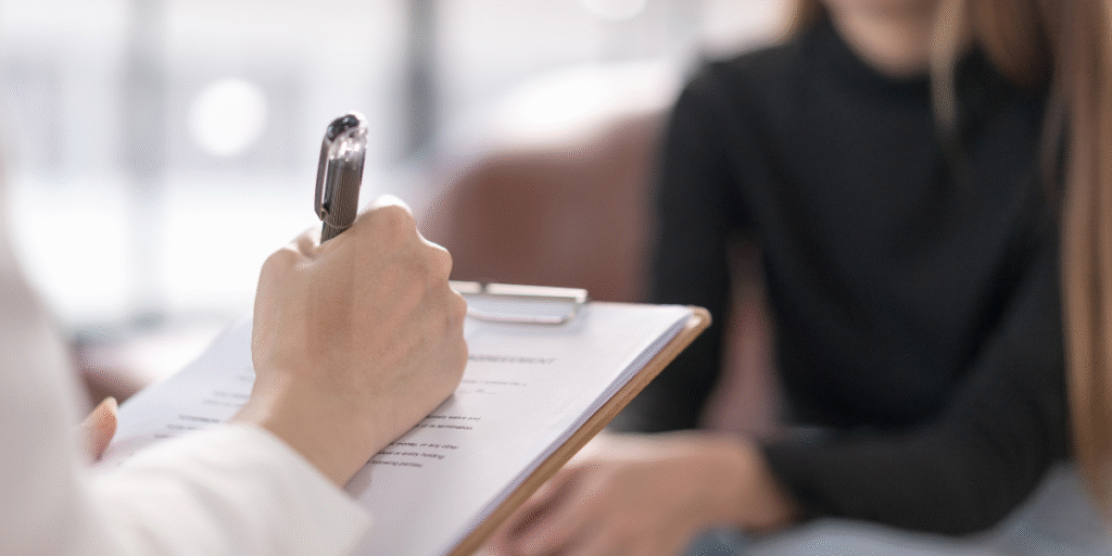 A woman writes on a clipboard while a man sits beside her, engaged in a discussion about career guidance.